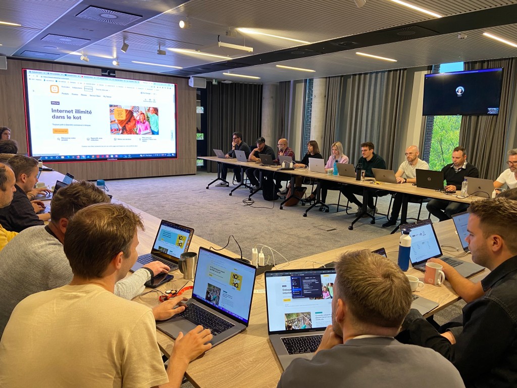 Group of 17 (visible) people attending the training with their laptops open, seating in a U table setup.