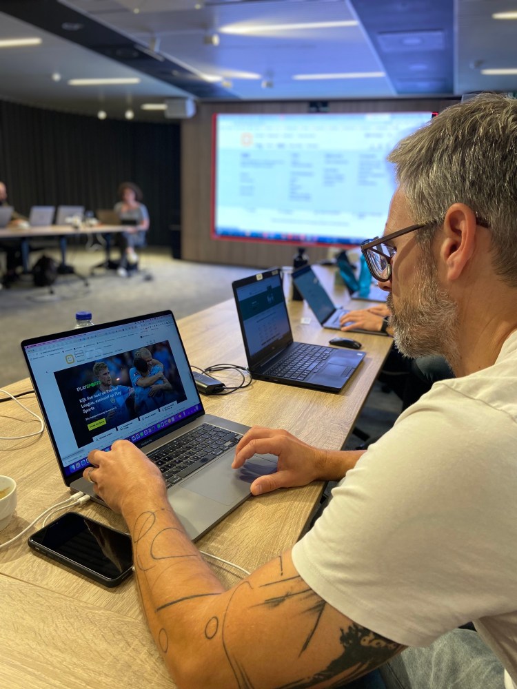 Person on a computer, keyboard testing a website in a classroom setup with 5 other computers and a projected screen in the background.