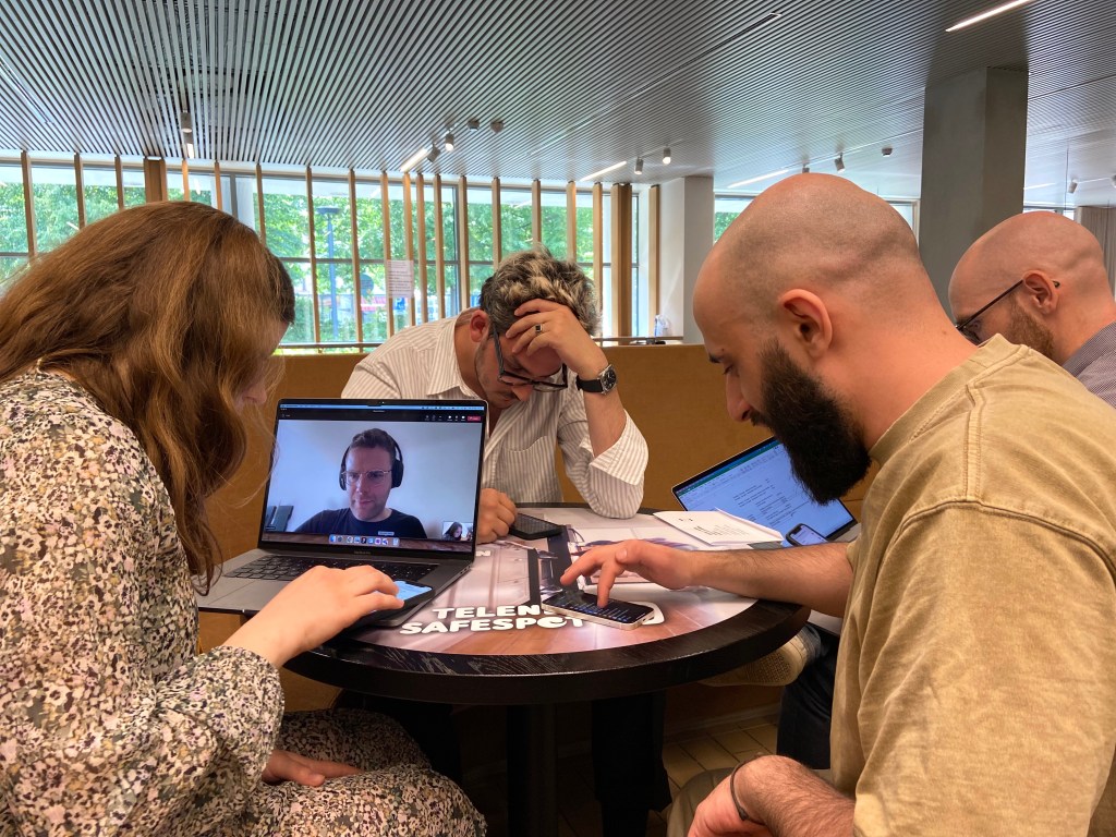 Group of 4 people seating at a round table with laptops and mobile phones, testing websites. 