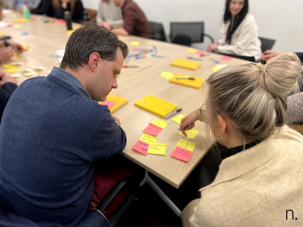 Two people at a table with post its, markers and paper during a workshop.