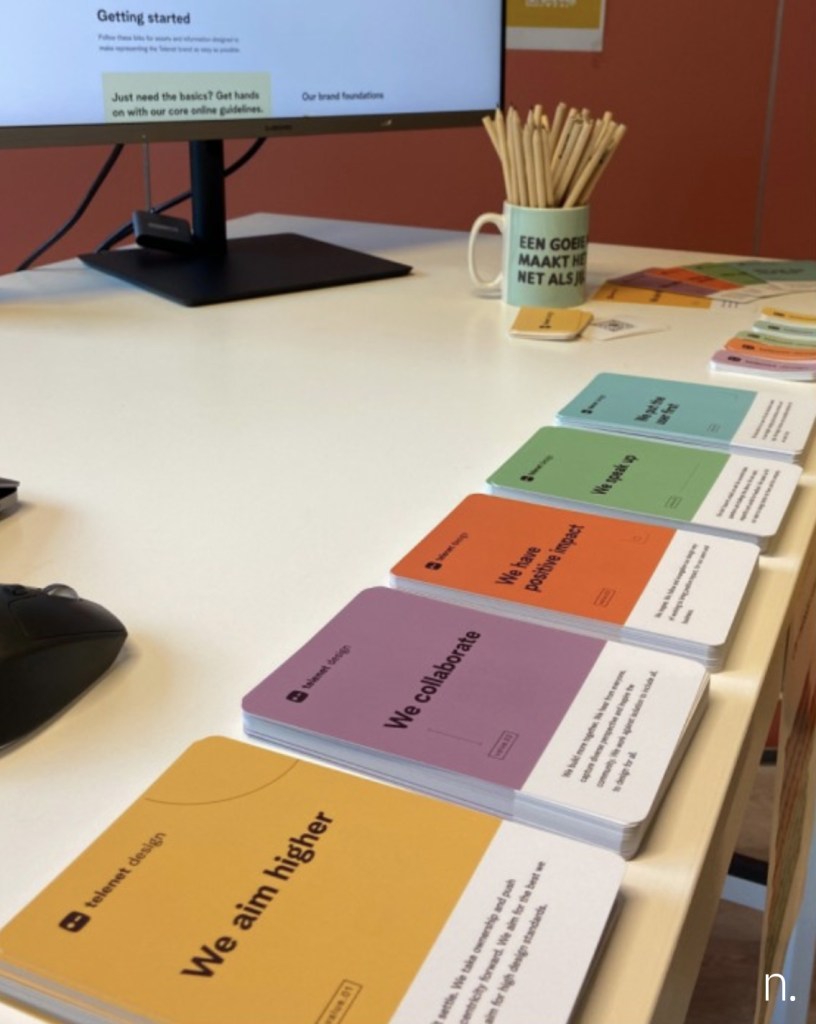 Set of 5 colourful stack of cards with a mug with pencils and a computer screen in the background.
